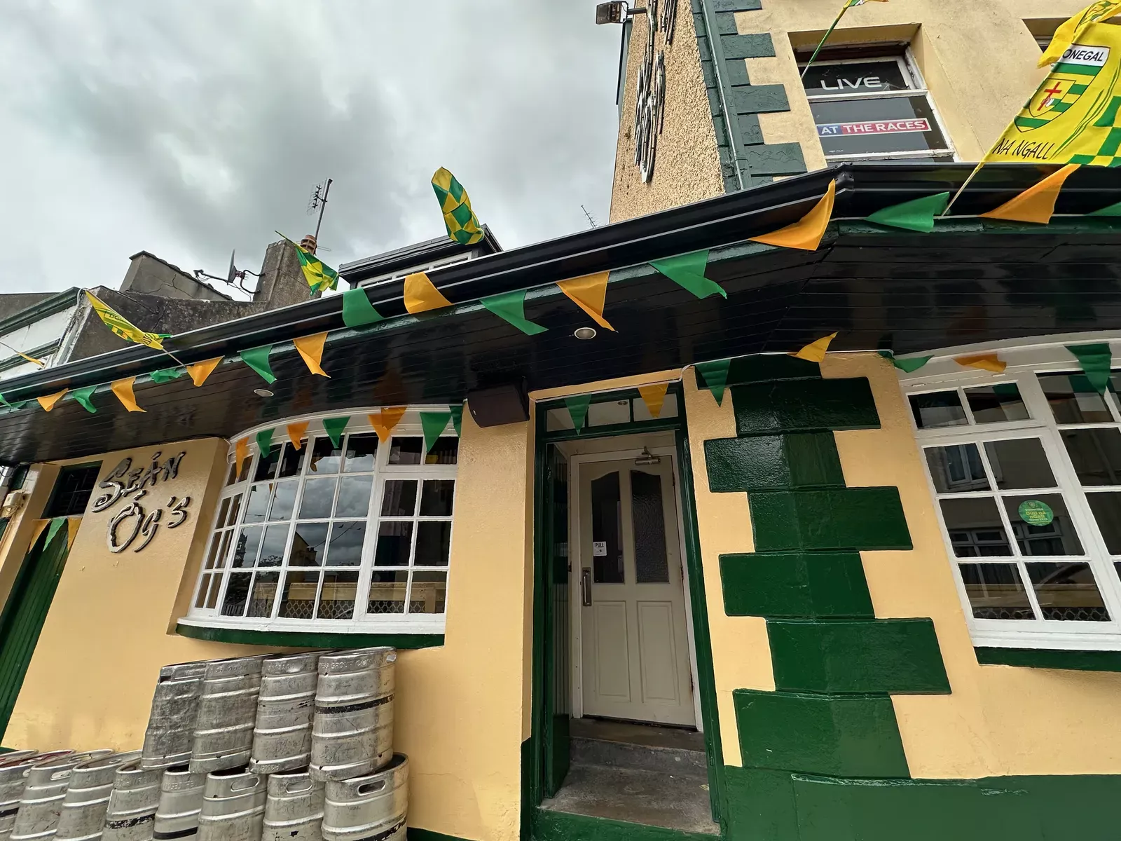 Sean Og's pub exterior with green and gold Donegal bunting, kegs stacked outside, and the pub name painted on the window